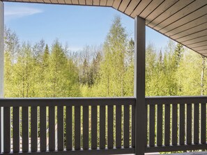 A covered outdoor area with a wooden railing, overlooking a dense forest. - Toivola 1 by Interhome (Sotkamo)