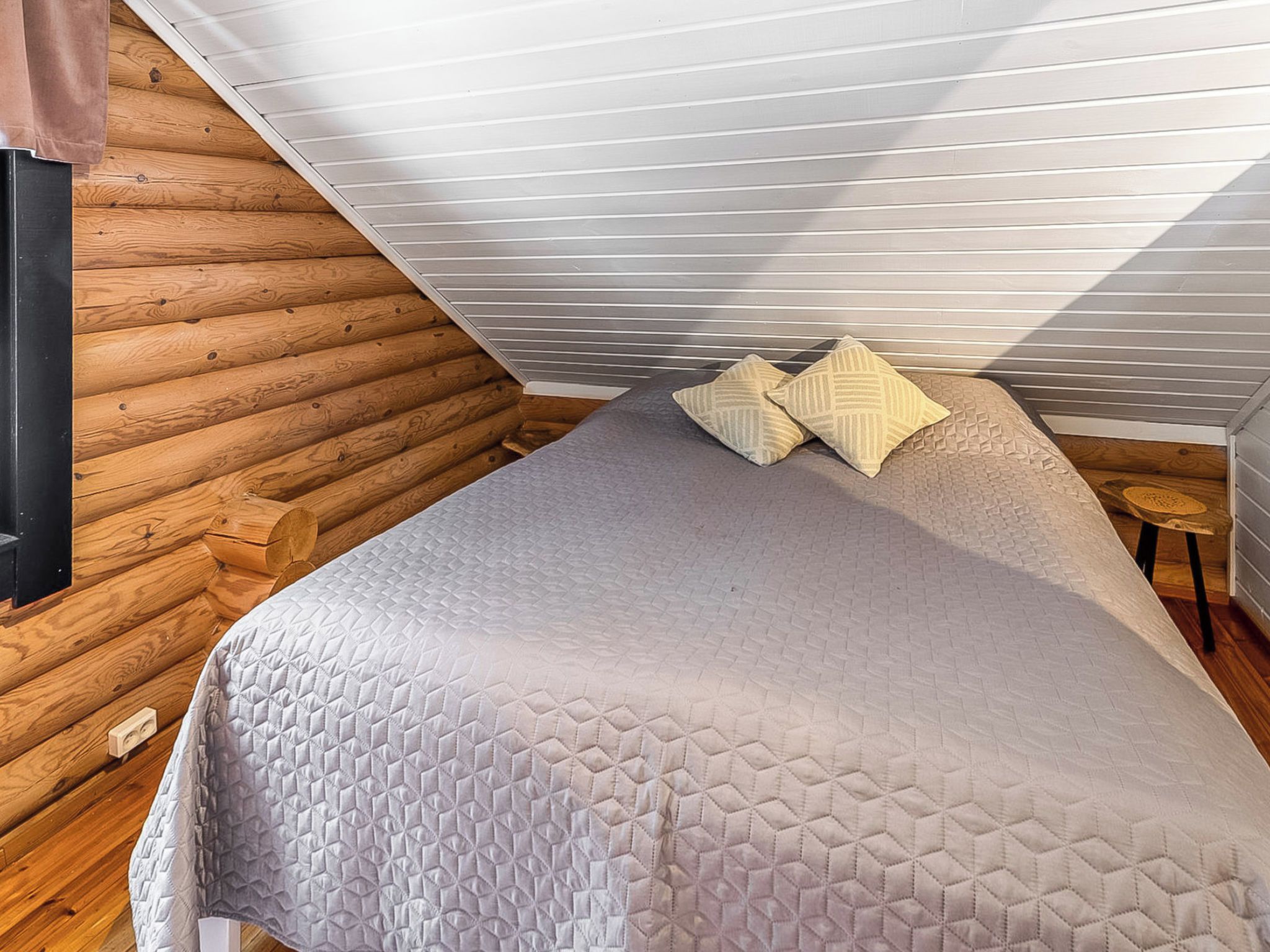 A bedroom with a sloped ceiling, wooden walls, a bed with a quilt, and two pillows.