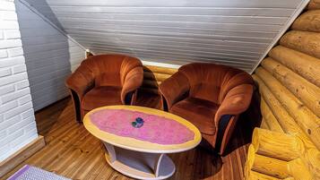 Een hoekzaak met twee bruine fauteuils, een klein rond tafeltje met een roze tafelkleed en houten vloeren.