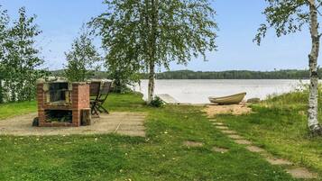 Een landschap aan het meer met een grill van baksteen en houten stoelen, een boot aan de oever en een helder uitzicht over het water.