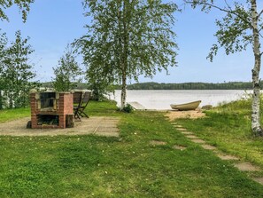 Een landschap aan het meer met een grill van baksteen en houten stoelen, een boot aan de oever en een helder uitzicht over het water.