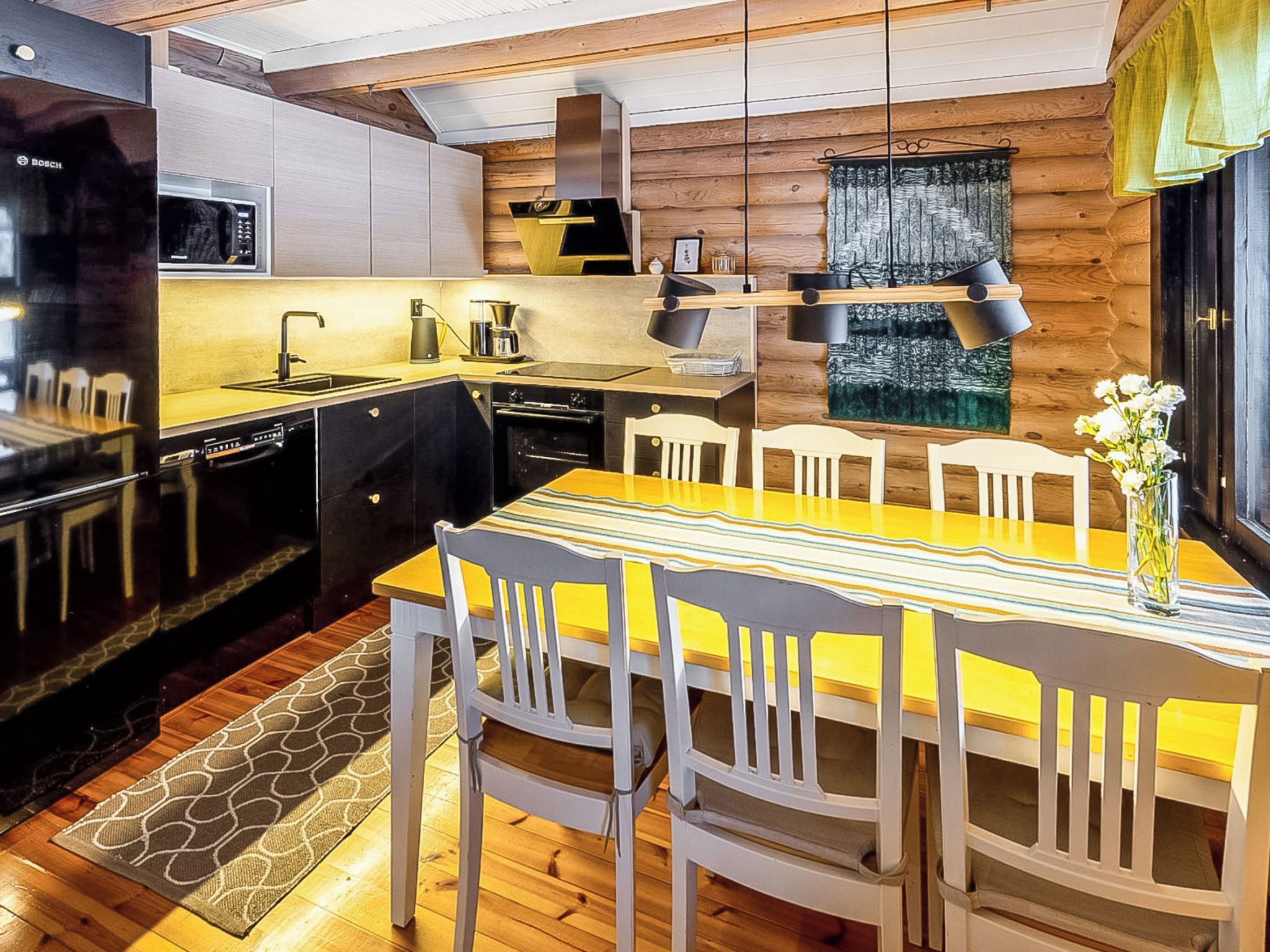 Cozinha compacta com eletrodomésticos modernos, sala de jantar com toalha de mesa listrada e piso de madeira.