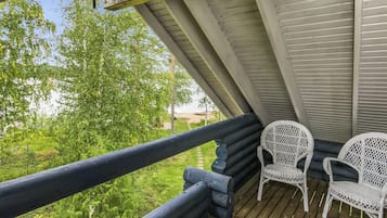A wooden deck with two wicker chairs, a railing, and a view of greenery.