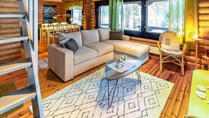 A log cabin interior with a beige sectional sofa, a dining area with a table and chairs, and a staircase. - Vacation home Tiira by Interhome (Puumala)