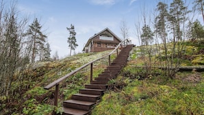 A wooden staircase leading to a cabin with a balcony, surrounded by greenery and trees. - Dominus by Interhome (Raasepori)