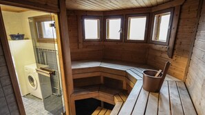 A wooden sauna with a bench, a bucket, and a washing machine visible in the adjacent room. - Dominus by Interhome (Raasepori)