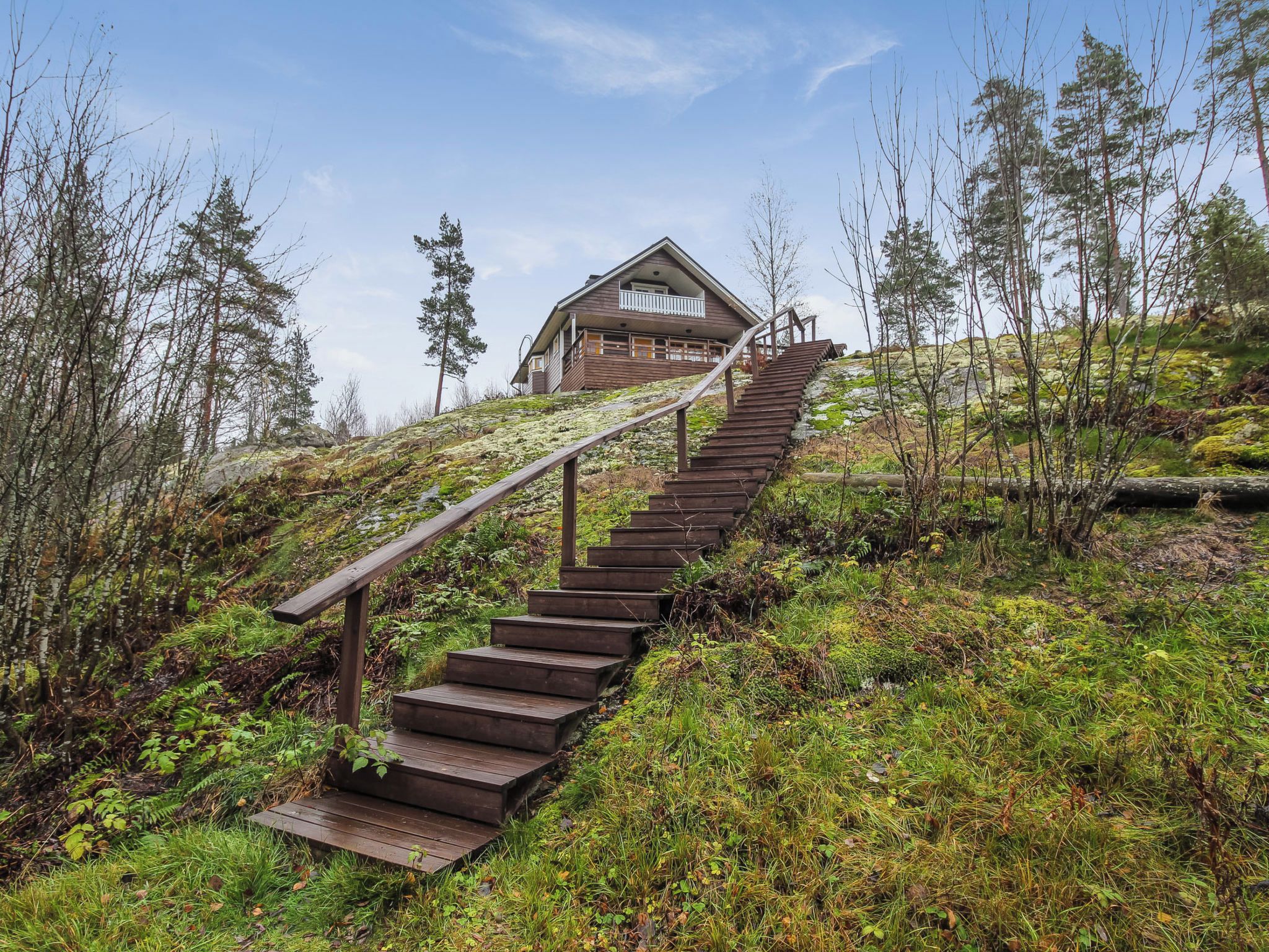 A wooden staircase leading to a cabin with a balcony, surrounded by a forested hillside.