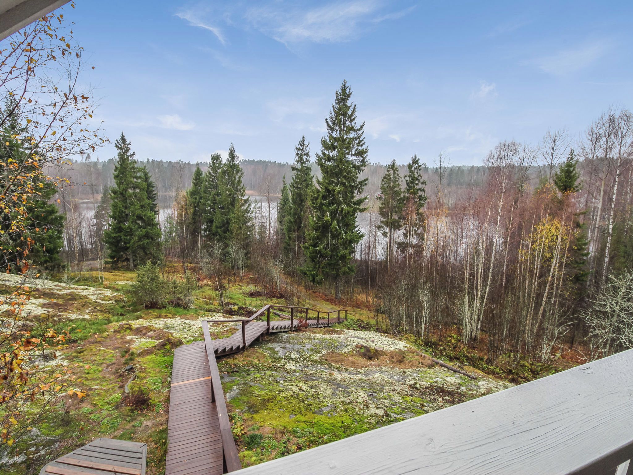 A wooden deck leading to a forested area with a lake in the background.