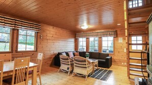 A cozy cabin interior with a wooden floor, a sofa, two wicker chairs, a dining table with chairs, and large windows. - Dominus by Interhome (Raasepori)
