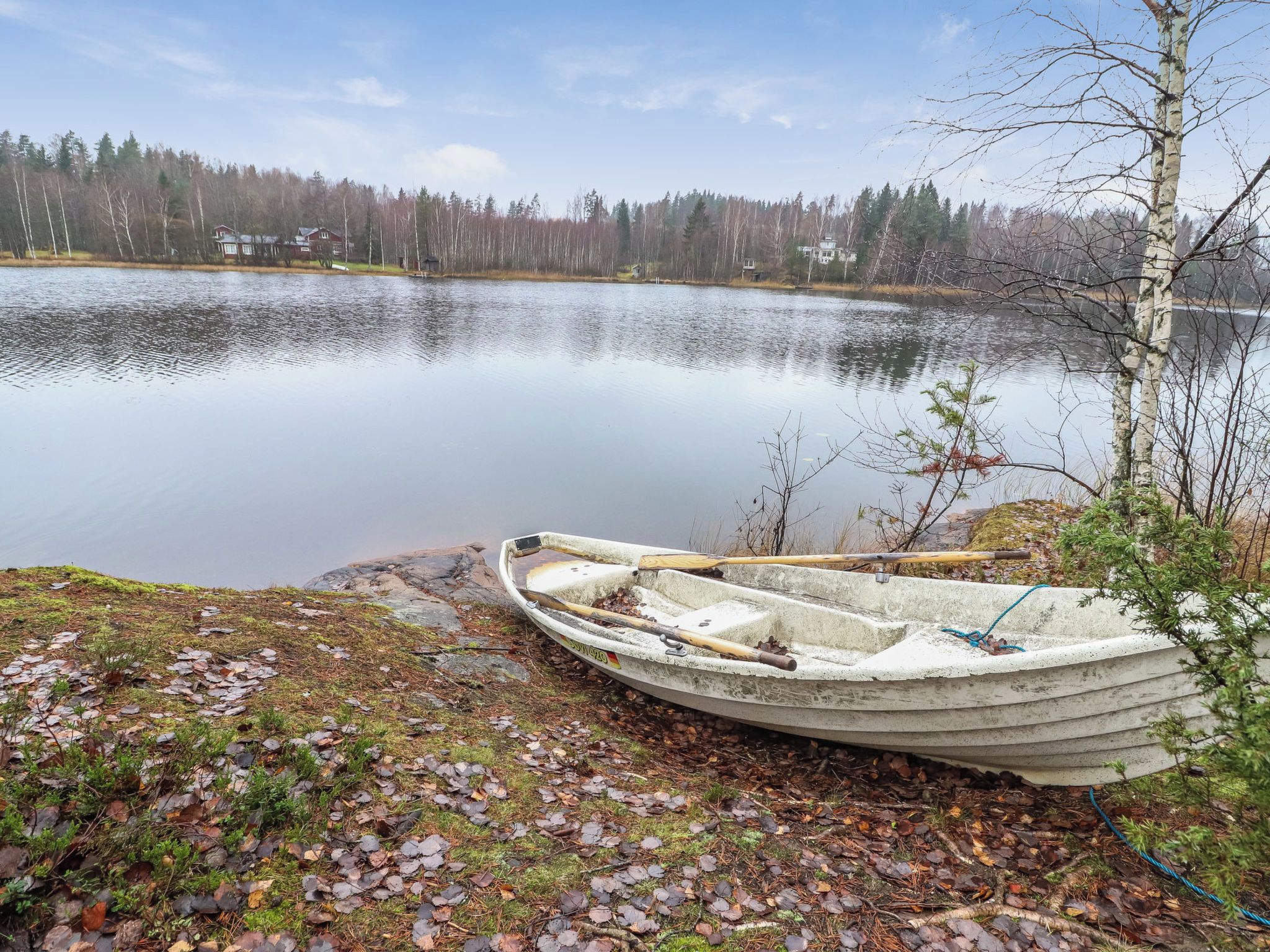 Un bateau à rames sur une rive rocheuse, au bord d’un lac paisible, avec des arbres en arrière-plan.
