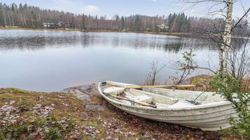 Un bateau à rames sur une rive rocheuse, au bord d’un lac paisible, avec des arbres en arrière-plan.