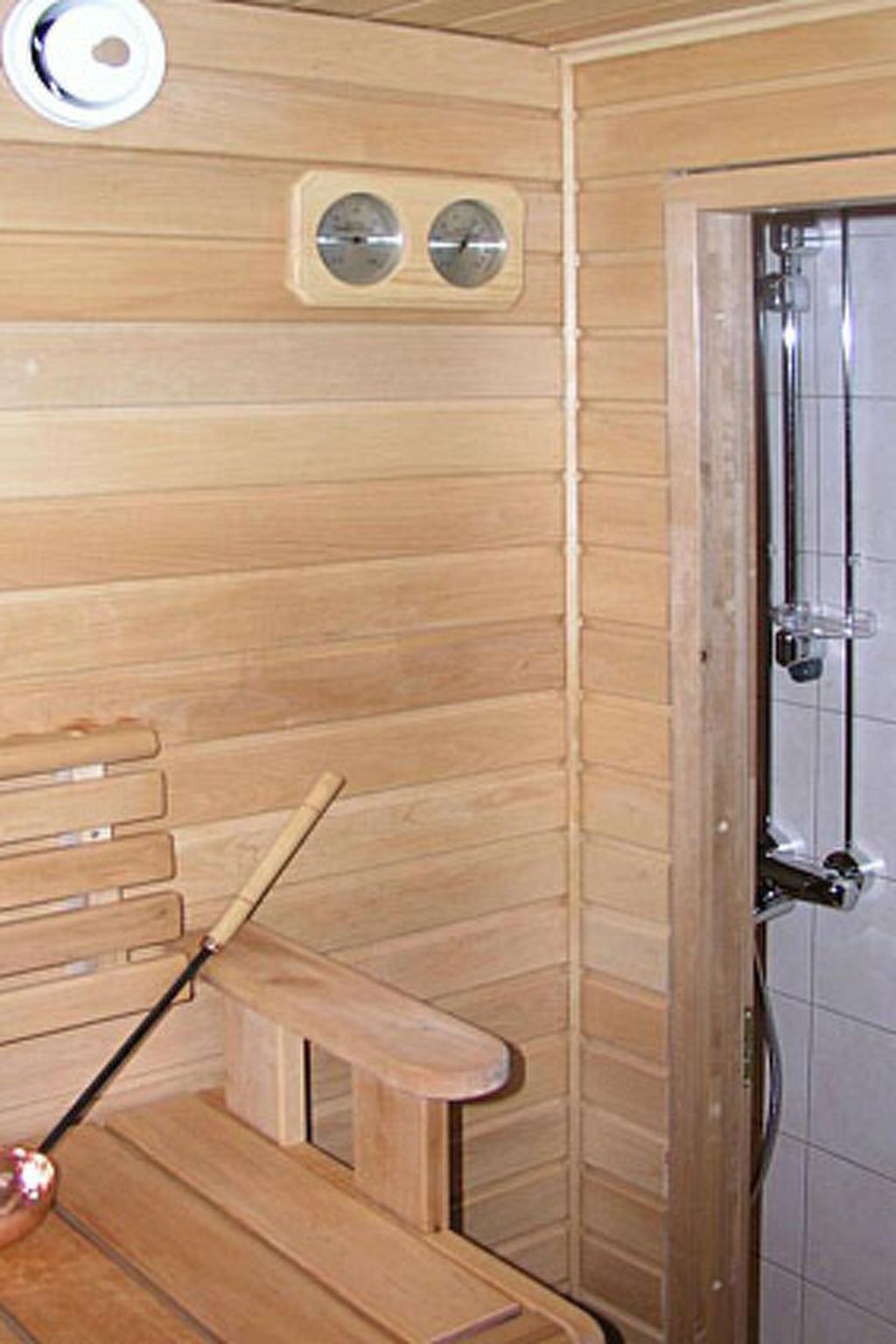 Uma sauna de madeira com bancos, uma porta e dois relógios fixados na parede.