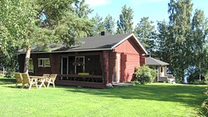 A red wooden house with a porch, surrounded by a well-maintained lawn and trees. - Rantamökki by Interhome (Luhanka)