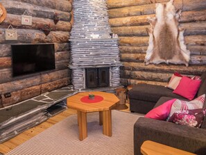 L’intérieur d’une cabane en rondins, avec une cheminée en pierre, un téléviseur à écran plat, une table en bois et un canapé avec des coussins.