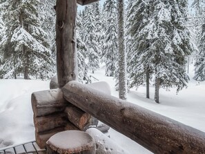 Une cabane en rondins de bois, dotée d’une terrasse enneigée et offrant une vue sur des arbres couverts de neige.