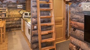 L’intérieur d’une cabane en rondins, avec une échelle en bois, un coin cuisine et une porte.