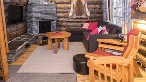 L’intérieur d’une cabane en rondins, avec une cheminée en pierre, un canapé, une table en bois et une chaise.