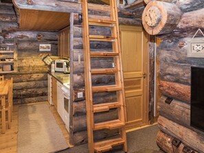 Interior de una cabaña de troncos con área de cocina, una escalera de madera y una puerta.