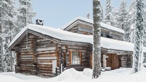 Une cabane en rondins avec une porte et des fenêtres en bois, entourée d’arbres couverts de neige.