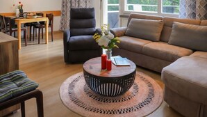 A modern living room with a sofa, a chair, a dining table with chairs, and a large window with a view of greenery. - Allod Park Haus C 301 by Interhome (Davos)