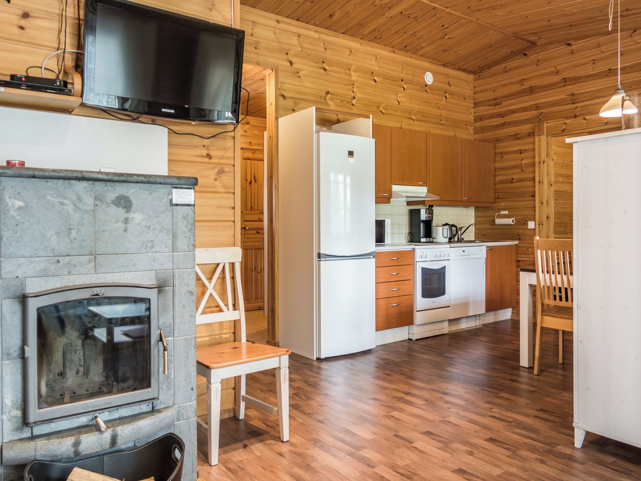 A wooden interior with a kitchen area featuring a refrigerator, oven, and coffee maker.