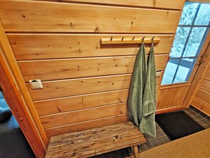 L’intérieur d’un chalet en bois, avec un banc, un porte-serviettes et une fenêtre donnant sur un paysage enneigé.