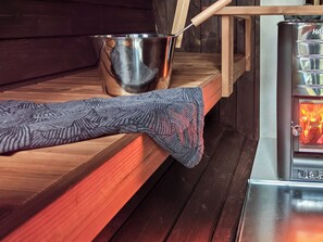 Een sauna met een houten bank, een metalen emmer en een verwarmingselement.