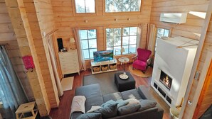 A cozy cabin interior with a fireplace, a sofa, a pink chair, and a TV. - Ihtingin koskikara by Interhome (Kuusamo)