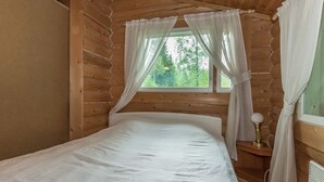 Une chambre dans un chalet en bois, avec un lit, une fenêtre avec des rideaux et une table de chevet avec une lampe.