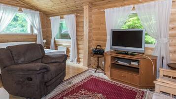 Une pièce chaleureuse dans un chalet en rondins, avec un canapé marron, un téléviseur posé sur un meuble en bois et un tapis rouge à motifs.