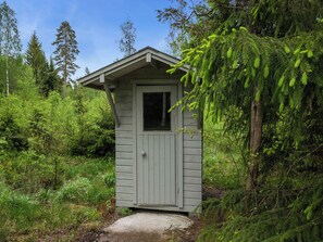 A small wooden cabin with a single door and window, surrounded by dense forest.