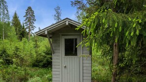 Une petite cabane en bois, d’un seul étage, entourée d’une forêt dense.