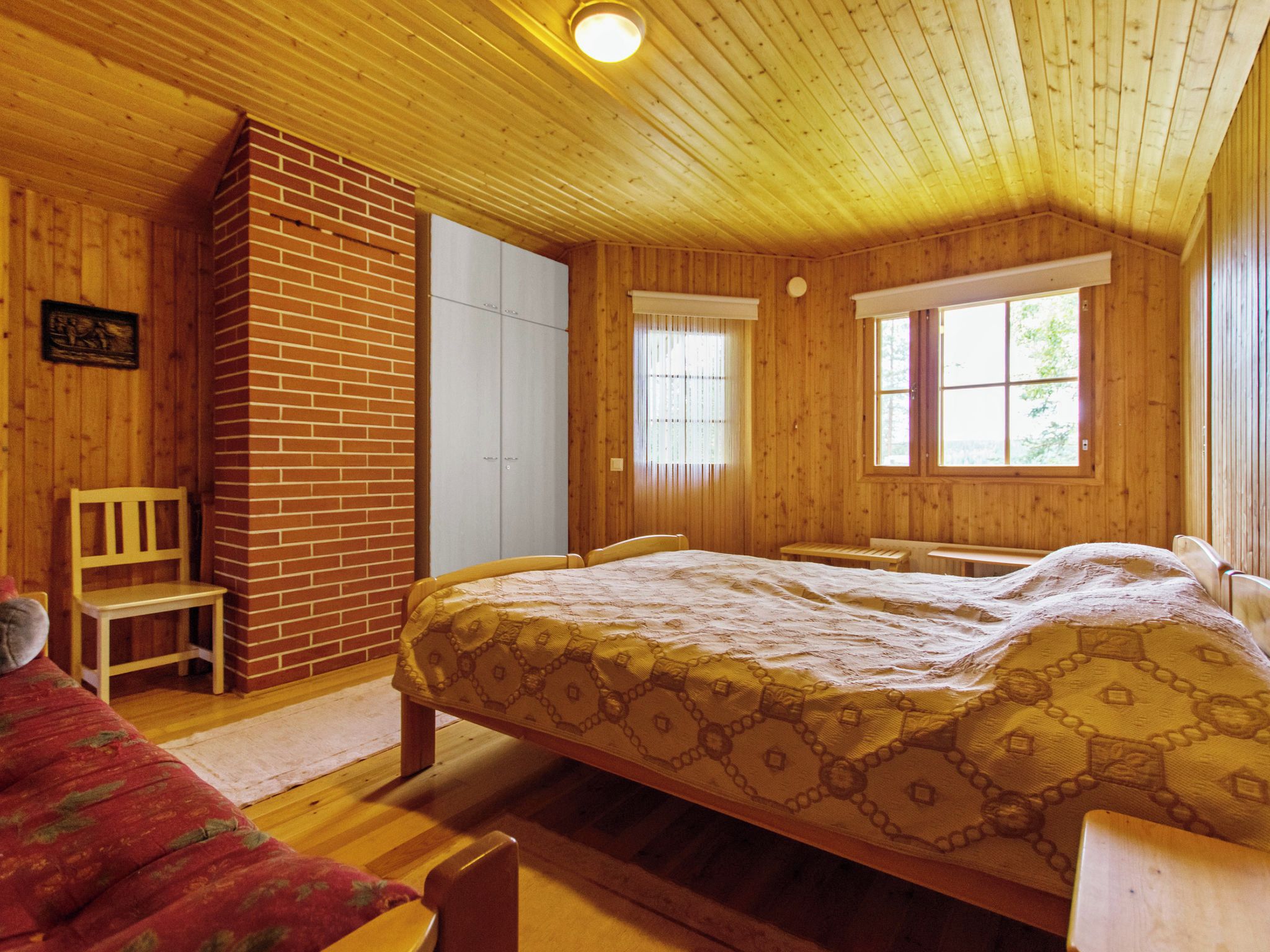 A wooden cabin bedroom with a bed, two chairs, a bench, and a window.