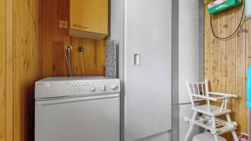 A compact kitchen with a washing machine, a refrigerator, and a small white chair.