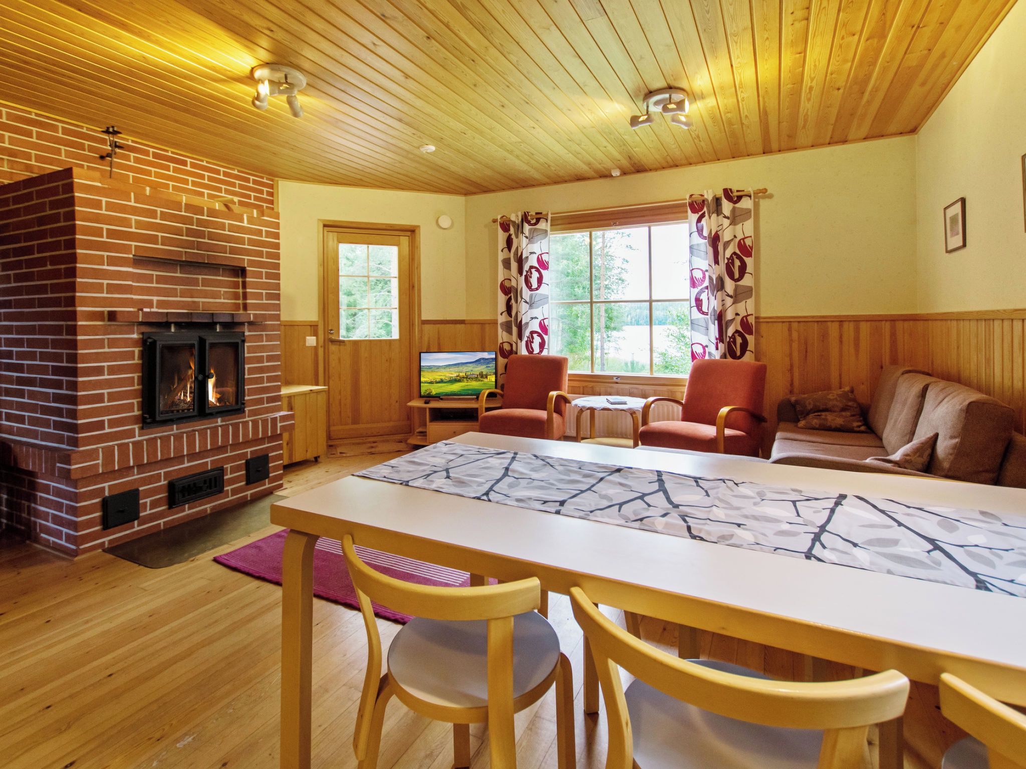 A cozy living room with a brick fireplace, wooden ceiling, and a dining area with a table and chairs.