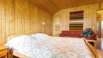 Ein Zimmer mit Holzboden, einem Bett, einer Bank und einem Stofftier.