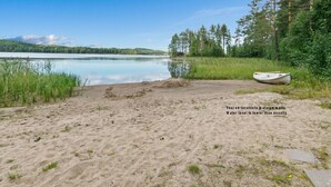 A sandy beach with a small boat, a calm lake, and a forested area.