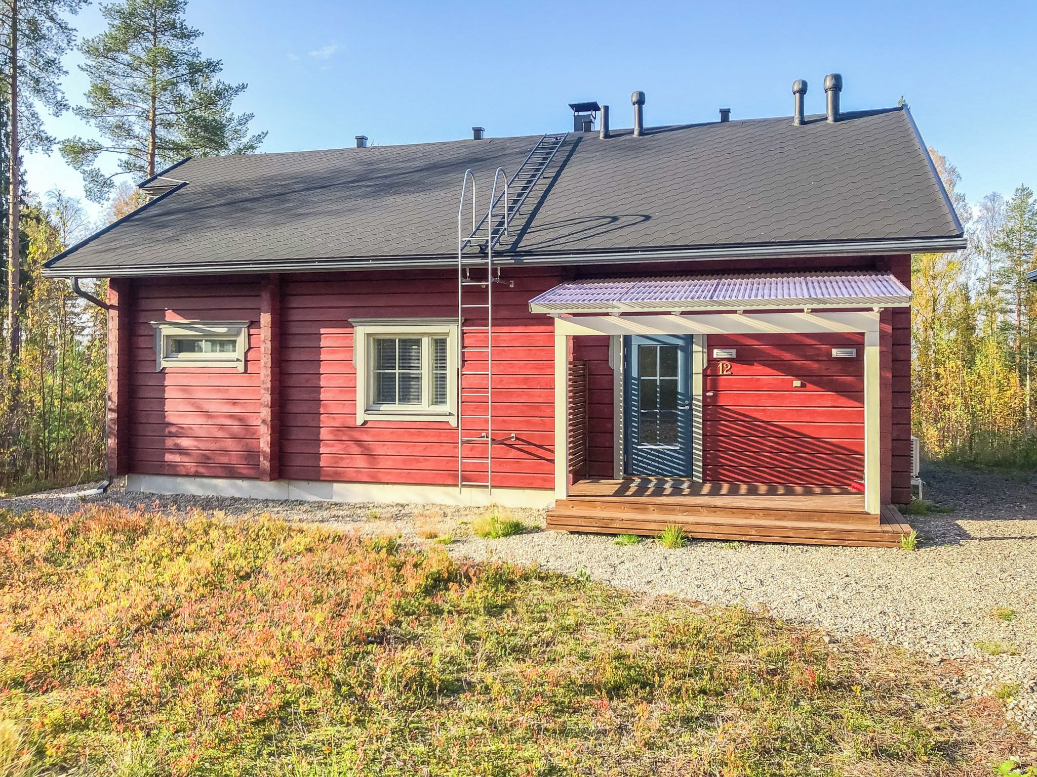 Een rood houten huis met een grijs dak, een houten veranda en een metalen ladder.