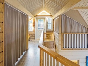 Un intérieur en bois avec un escalier menant à une mezzanine, une porte avec une fenêtre et un lampadaire.