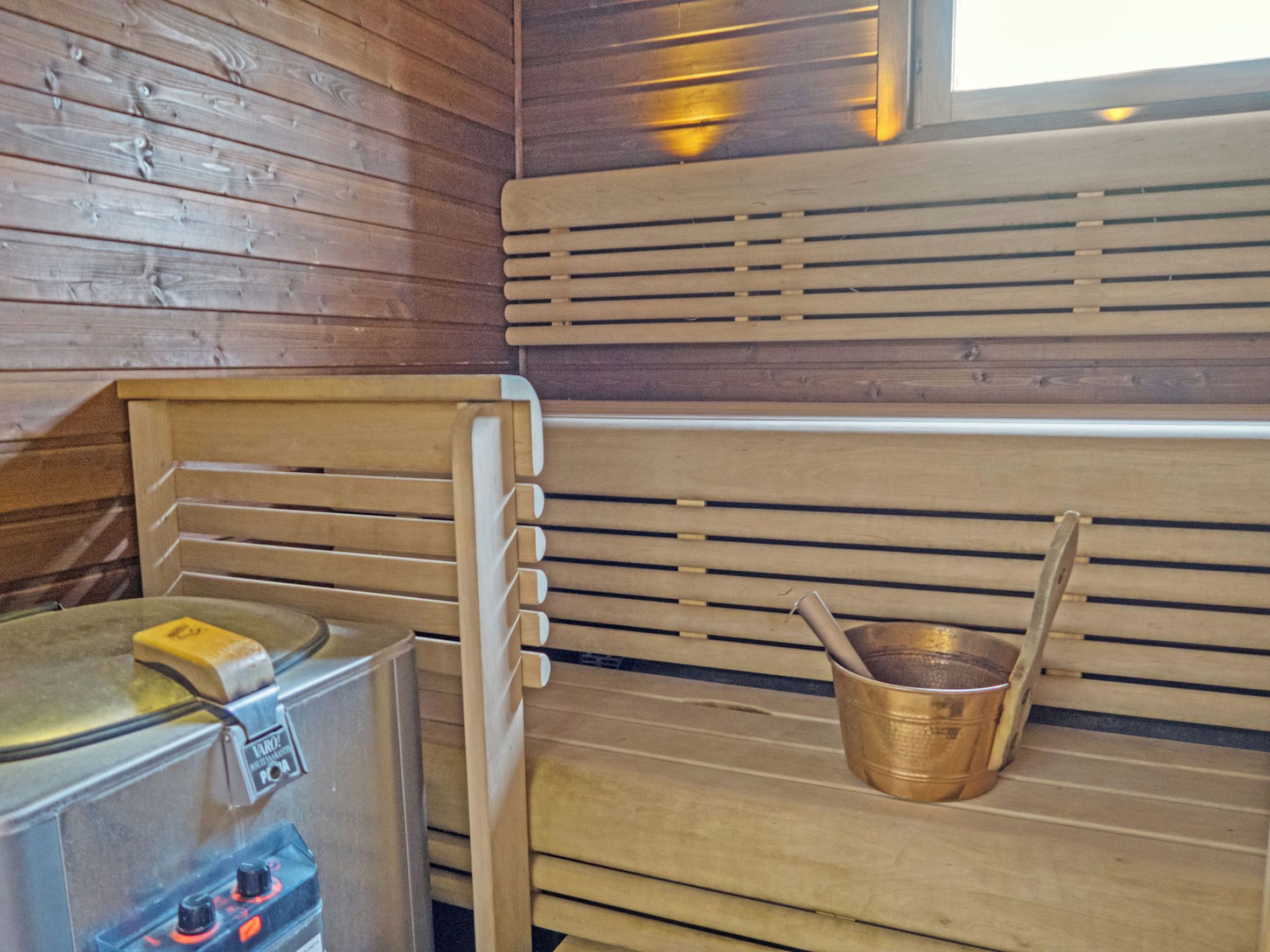 Un sauna avec des bancs en bois, un appareil de chauffage pour sauna et un seau en cuivre.