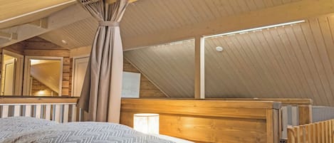 Een slaapkamer met een schuine plafond, houten wanden, een bed met beddengoed met een patroon en een raam.