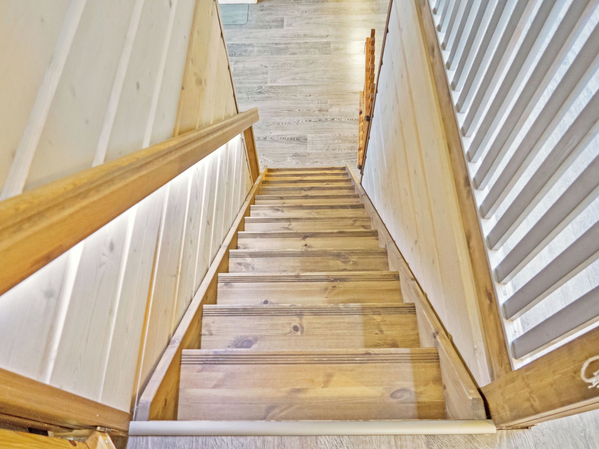 Una escalera de madera de diseño moderno que conduce a una habitación con piso de tonos claros.
