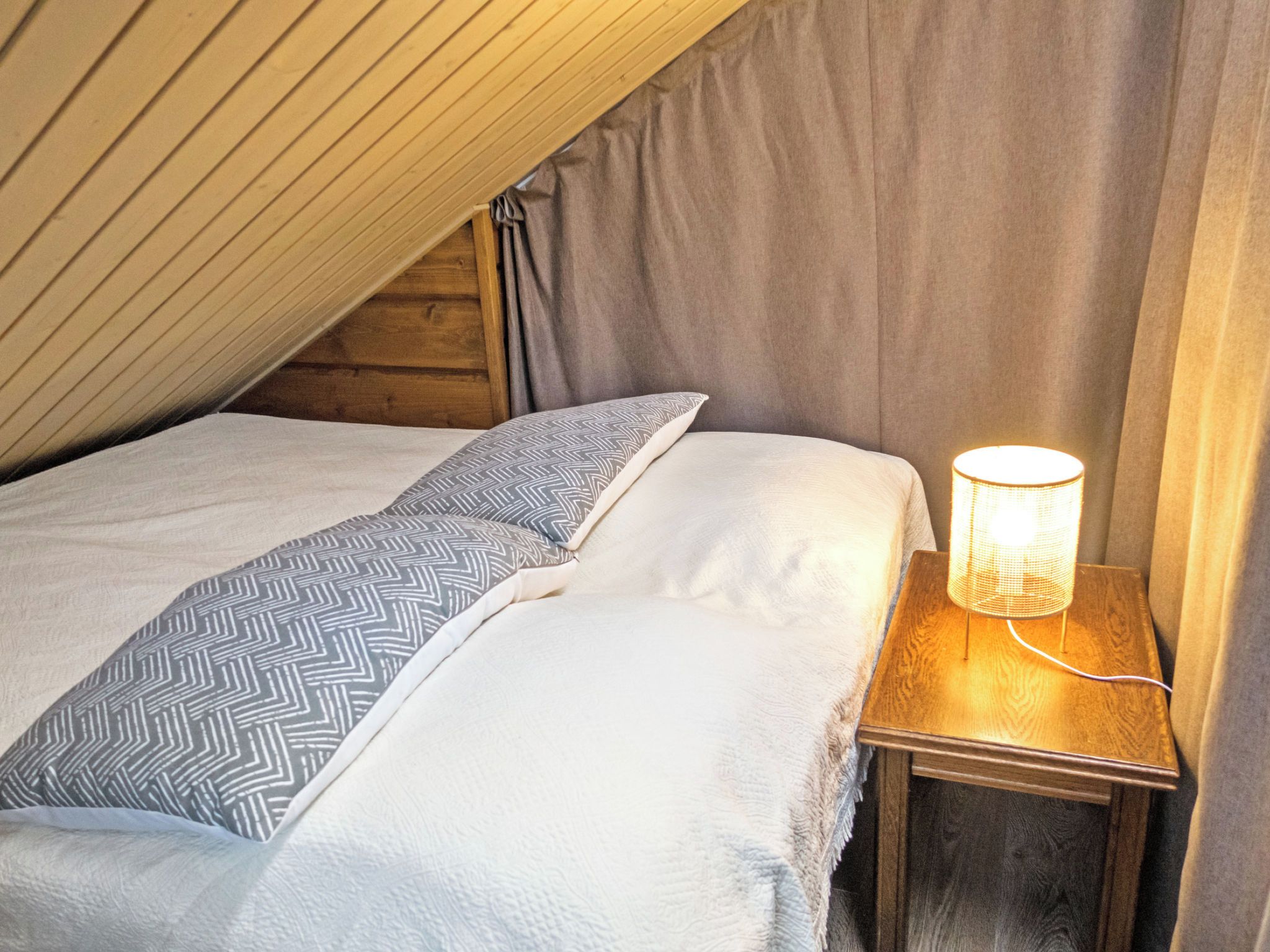 Ein Schlafzimmer mit schrägem Dach, einem Bett mit gemusterten Kissen und einer Nachttischlampe.