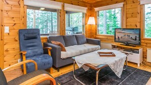 Interior acogedor de una cabaña con paredes de madera, un sofá, una silla, una mesita y un televisor.