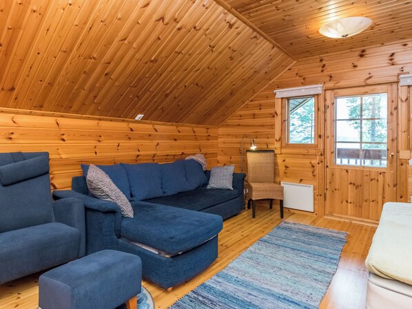 A cozy cabin interior with a wooden ceiling, a sofa set, a chair, and a window with a view of trees. - Metsola / huilinpaikka by Interhome (Kerimäki)