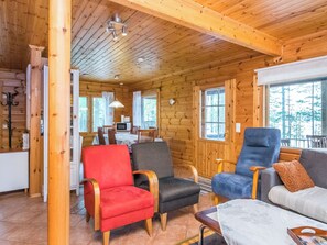 A cozy cabin interior with wooden walls, a dining area, and a living room with a sofa and chairs. - Metsola / huilinpaikka by Interhome (Kerimäki)