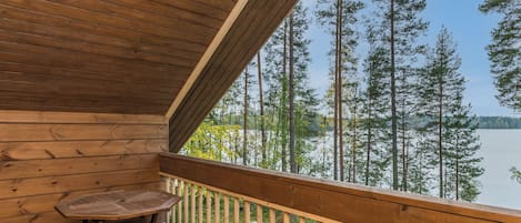 A wooden deck with a table and a chair, overlooking a forest and a lake.