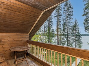 A wooden deck with a table and a chair, overlooking a forest and a lake. - Metsola / huilinpaikka by Interhome (Kerimäki)