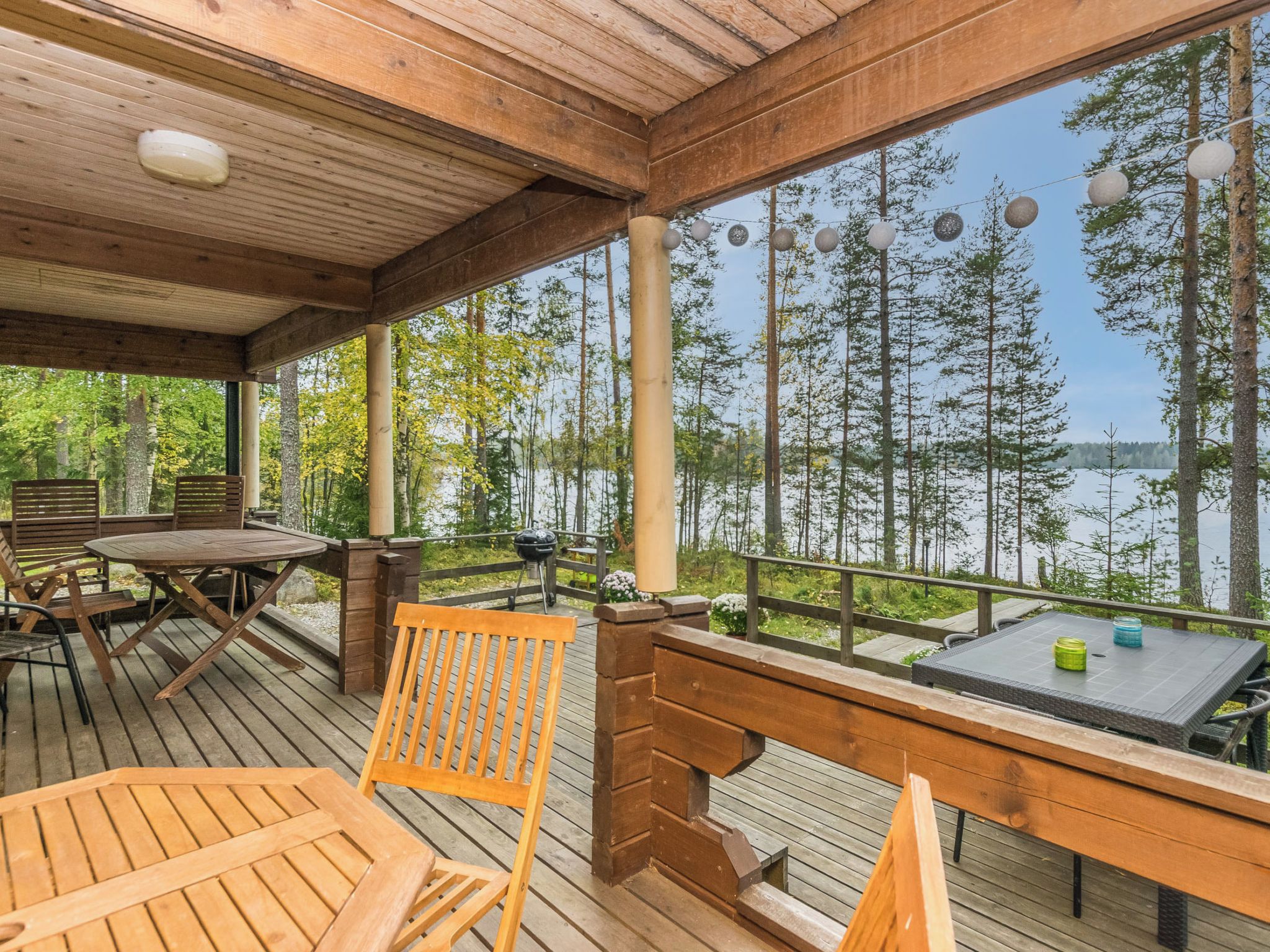 A wooden deck with outdoor furniture, a grill, and a view of a lake surrounded by trees.
