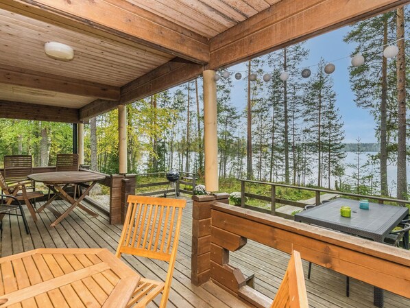 A wooden deck with outdoor furniture, a grill, and a view of a lake surrounded by trees. - Metsola / huilinpaikka by Interhome (Kerimäki)